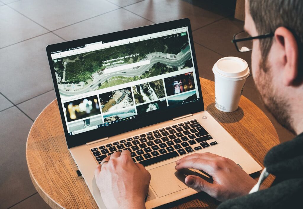 Man working on a laptop in a modern workspace with a coffee cup nearby, showcasing online activity.